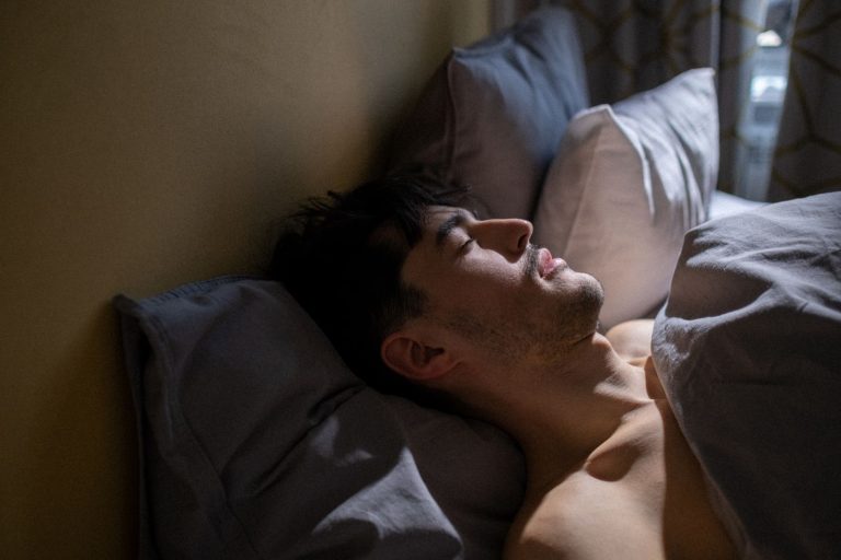 Hombre durmiendo boca arriba en la cama con luz suave de mañana.